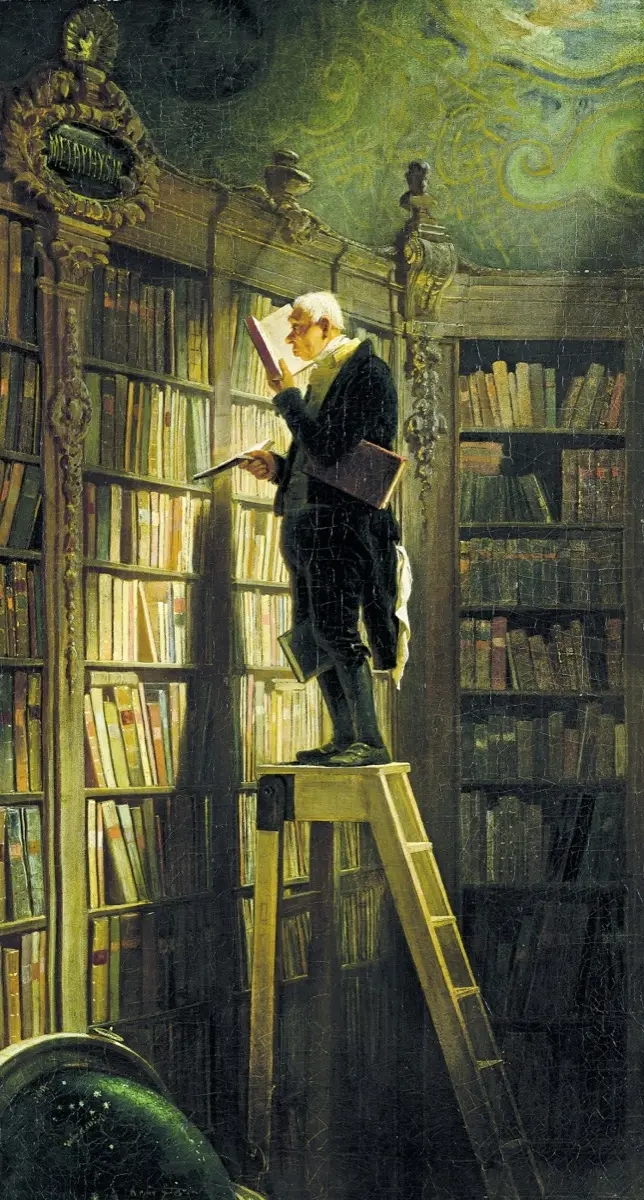 A man on a library ladder, absorbed in a book
